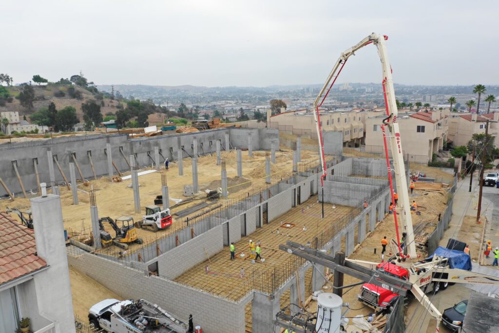 Concrete podium construction with pump truck placing slab and crews working