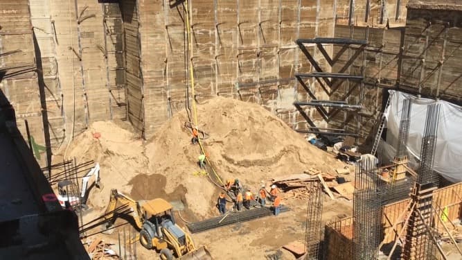Construction crew working inside deep excavation with shoring and heavy equipment