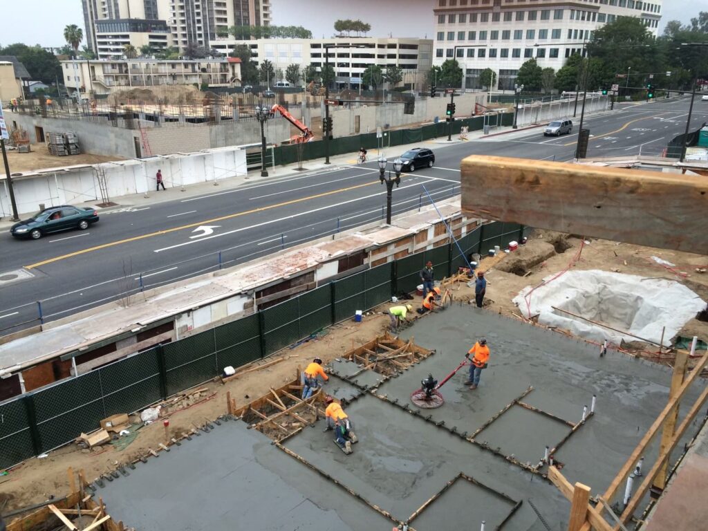 Concrete crew finishing slab sections beside active city street and traffic