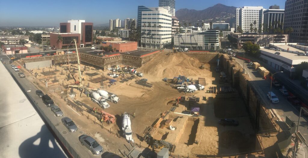 Aerial view of deep excavation with concrete pumps and trucks placing foundations