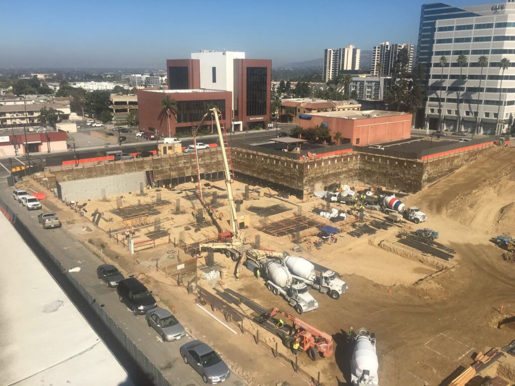Wide aerial view of urban construction site with excavation, pumps, and concrete crews