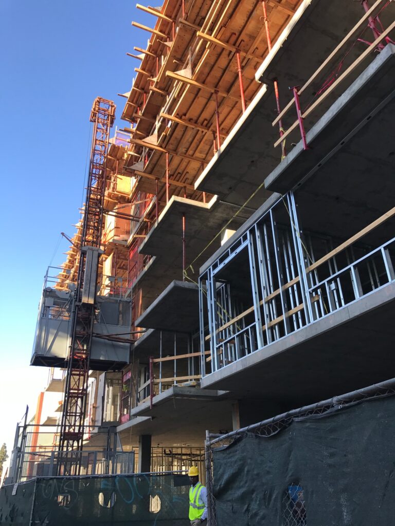 Street-level view of concrete mid-rise under construction beside completed office building