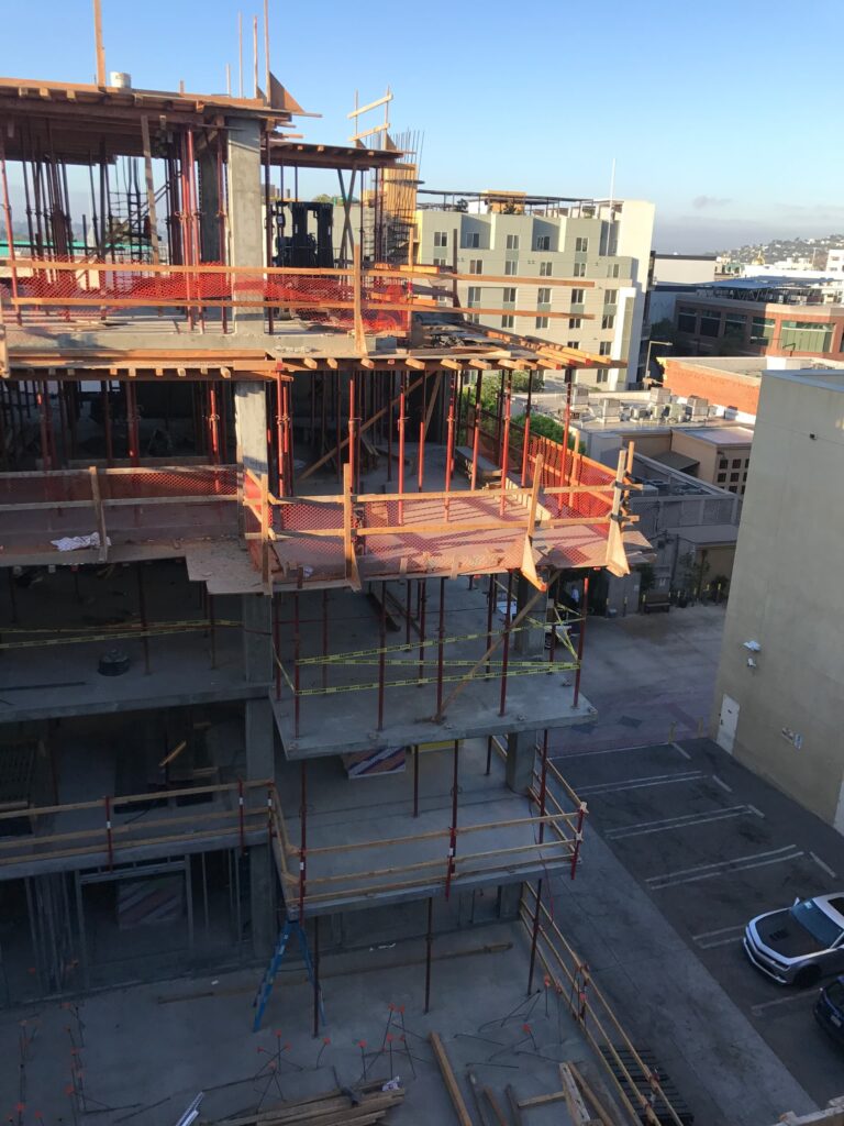 Multi-story concrete building under construction with scaffolding and perimeter safety rails